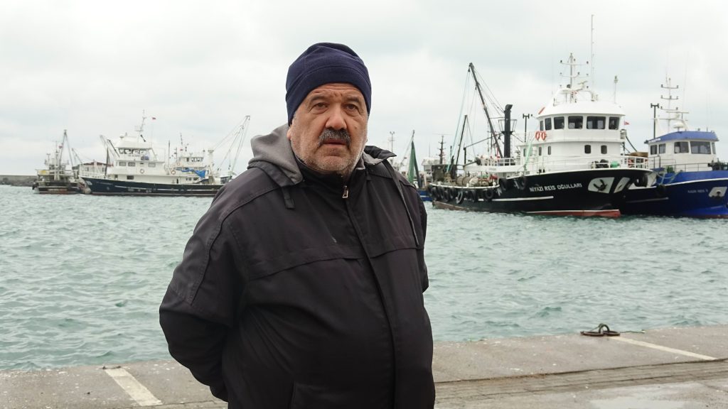 Atıf Malkoç, Karadeniz’de geç soğuma nedeniyle hamsi avcılığındaki belirsizliği değerlendirirken balıkçı tekneleri önünde görüntülendi.